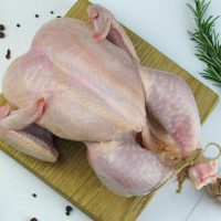 a raw chicken on a cutting board next to a slice of lemon