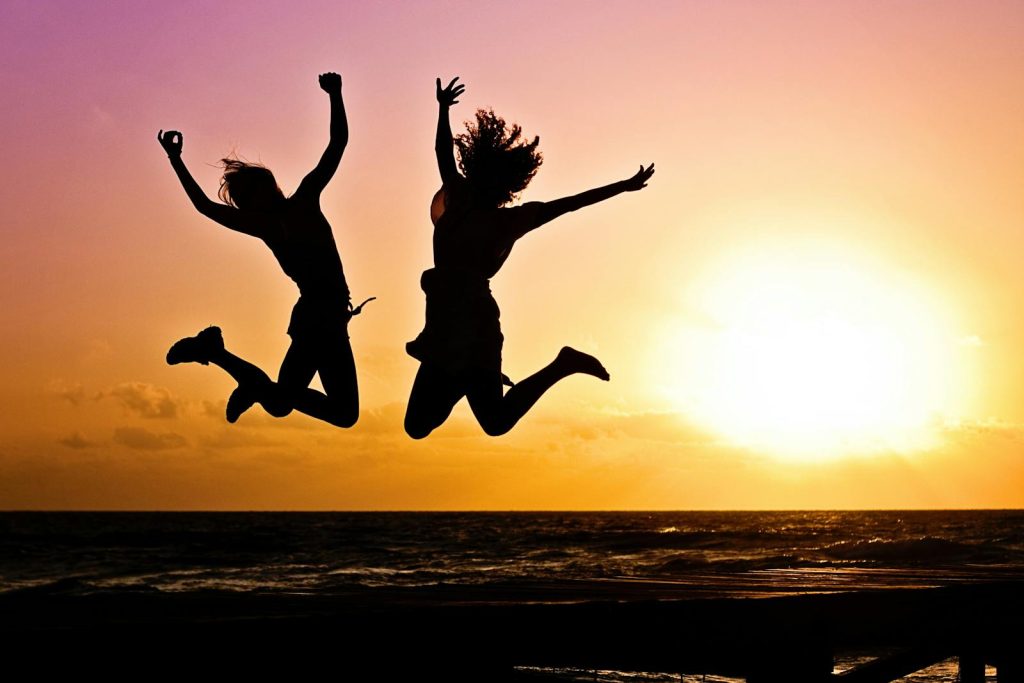 Winning Swertres or 3D Lotto- Silhouettes of two people joyfully jumping on a beach during a vibrant sunset.